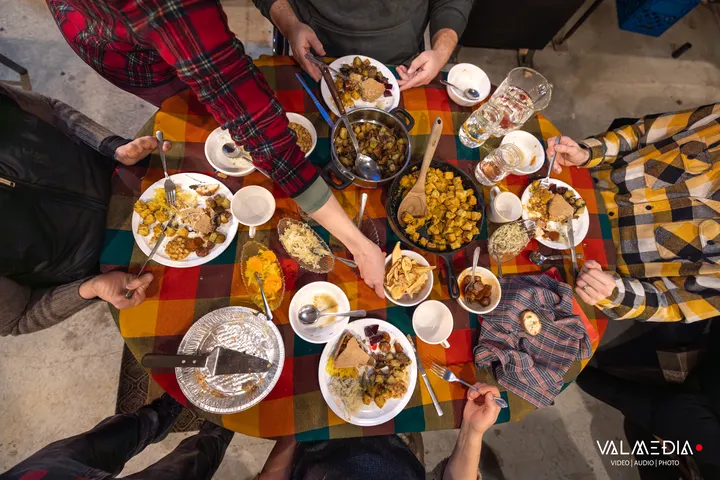 Une tablée vue du dessus : plats, assiettes et mains autour d'une nappe à carreaux