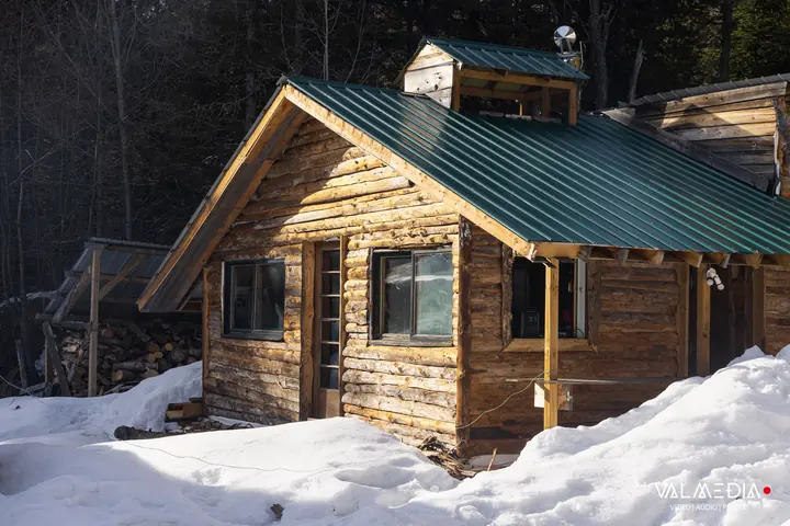 La cabane en bois rond, au toit vert, dans la neige